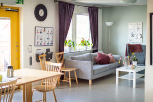 Vardagsrum i den gemensamma lägenheten. Här finns soffa, fotölj och TV. Ett kök med köksbord och stolar finns också. Här äter eleverna ihop och träffas för andra aktiviteter.